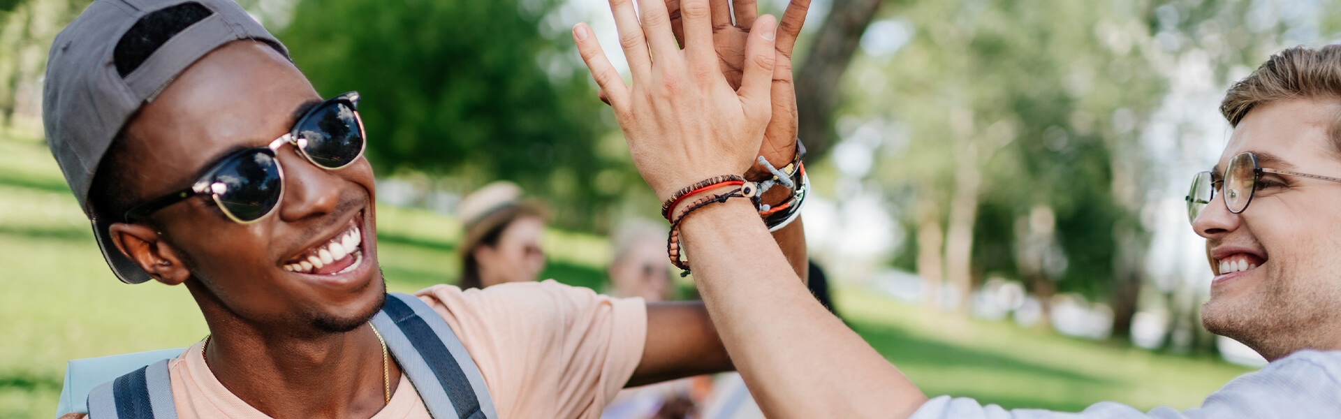 a young Black man wearing sunglasses smiles and high fives a white friend